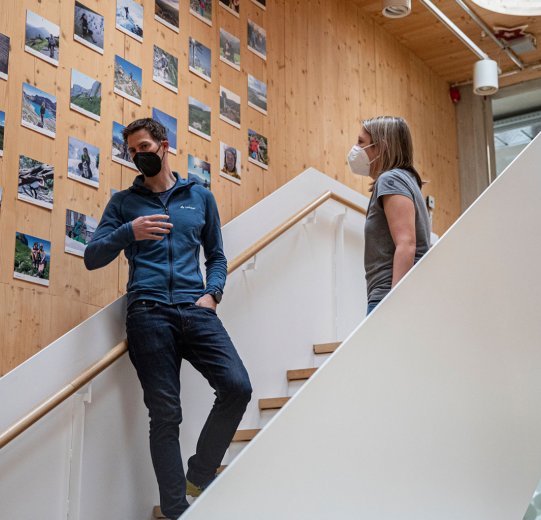 Eine Wand vollerFotografien von Vaude-Mitarbeitenden in einem Treppenaufgang.