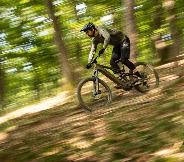 Berno heizt mit dem Turbo Levo 4 E-MTB durch den Wald. Die Umgebung ist durch die Mitzieheraufnahme unscharf, nur Bike und Rider sind scharf und erkennbar. 