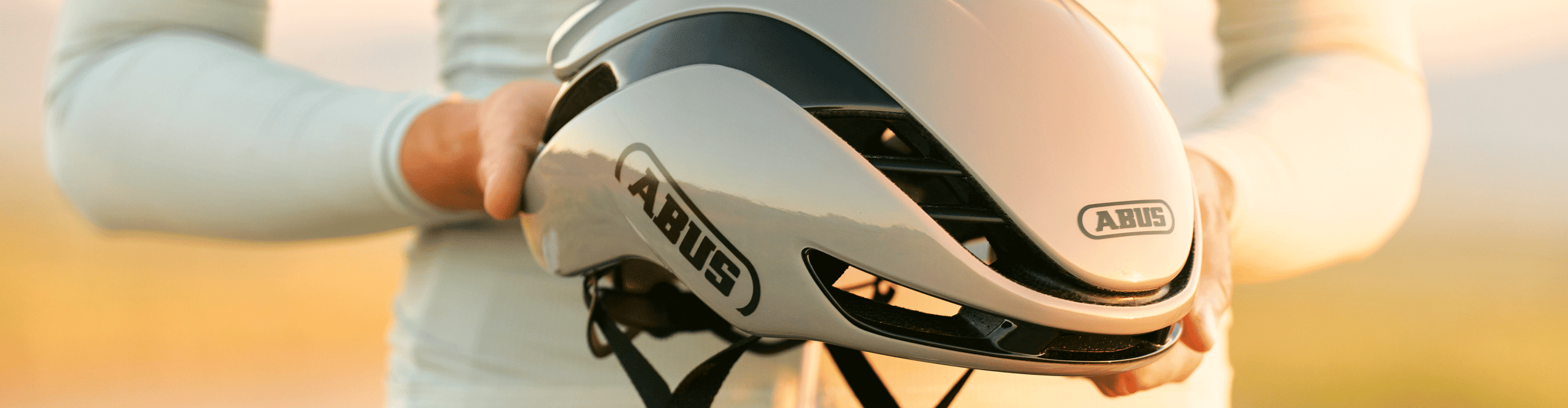 Cycliste sur route tenant un casque de vélo aérodynamique ABUS argenté dans ses mains.