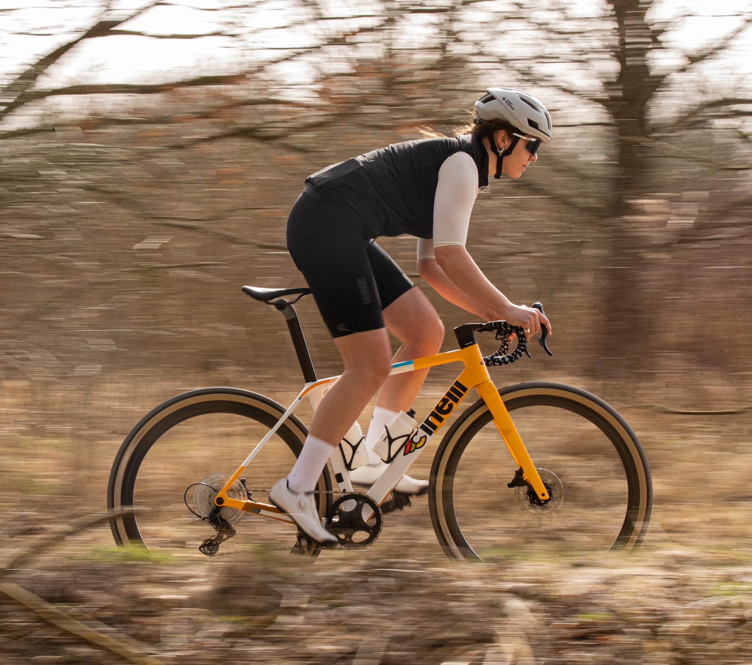 Fahrerin auf einem gelben Cinelli Zydeco II Gravelbike fährt dynamisch durch einen herbstlichen Wald, der Hintergrund ist in Bewegungsunschärfe.
