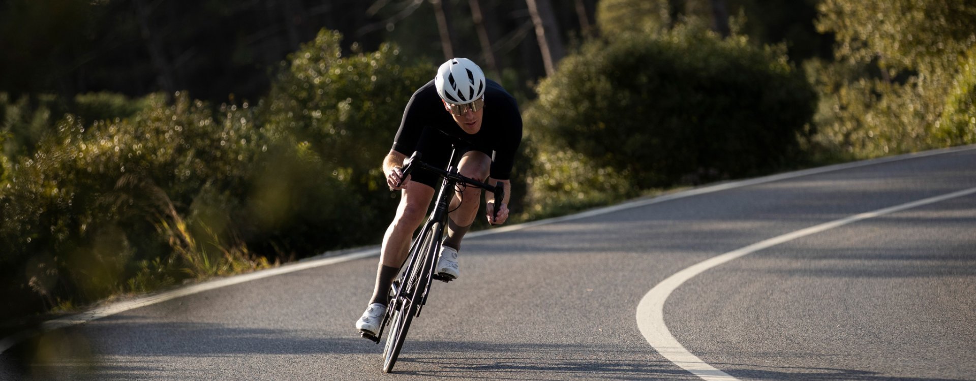 Sergej aus dem bc Service-Team fährt auf einem Rennrad eine Straße hinab. Er hat eine aerodynamische Position eingenommen.