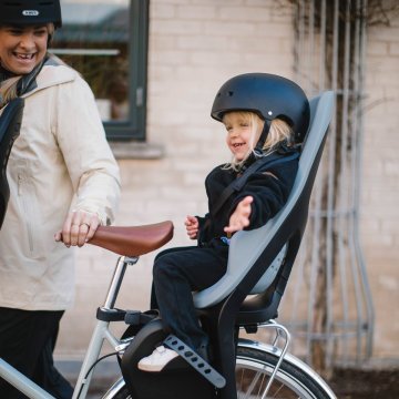 Toddler sitting in a rear-mounted child bike seat with helmet and safety harness for everyday transport.