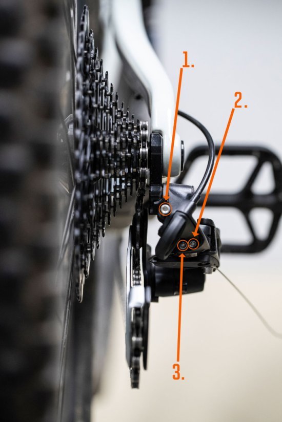 The MTB rear derailleur is shown from the rear. The limit screws H and L as well as the B-screw are marked with orange arrows. 
