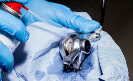 Gros plan d’une personne portant des gants bleus pulvérisant du nettoyant pour freins sur un étrier de frein de vélo tout en tenant un chiffon en dessous.