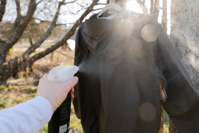 Eine Hardshelljacke hängt auf einem Bügel an einem Baum. Im Gegenlicht sieht man den Sprühnebel aus dem Zerstäbuer mit Imprägnierlösung