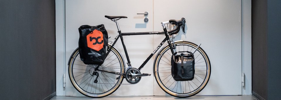 Surly Long Haul 28" mit Gepäckträger, Lowrider und den passenden Taschen vor der Werkstatttür bei bike components