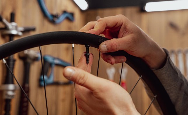 Main insérant une valve tubeless dans une jante de vélo et la fixant avec un écrou de serrage.