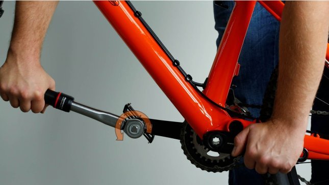 Mechaniker:in zieht das Pedal mit einem Drehmomentschlüssel an und hält mit dem anderen Kurbelarm gegen.