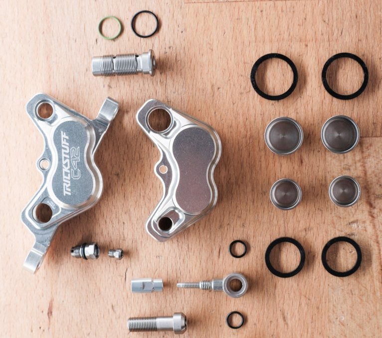 Las piezas de una pinza de freno Trickstuff C42 están distribuidas sobre una superficie de madera de haya.