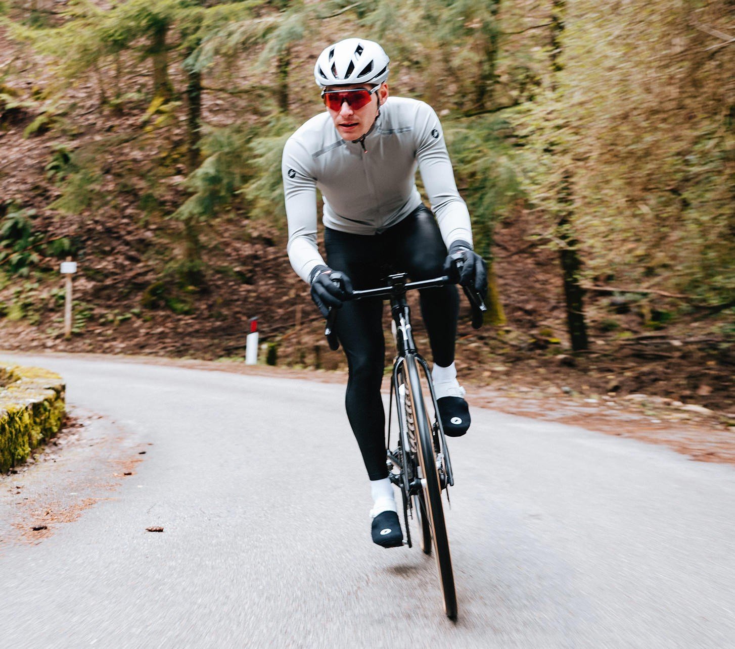 Cycliste sur route en vêtements Castelli pour l’automne et l’hiver roulant sur une route sinueuse en forêt.