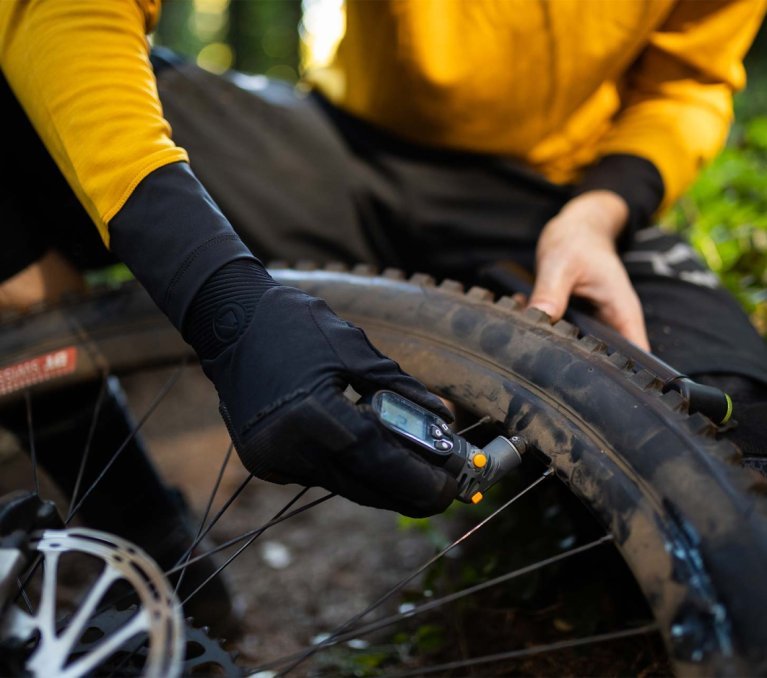Ciclista de montaña midiendo la presión de un neumático de MTB con tacos usando un medidor digital.