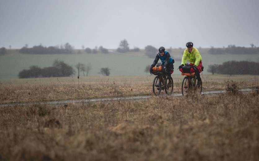 2 Teilnehmer fahren bei heftigem Regen. An ihnen spritzen Wasser und Matsch hoch. 