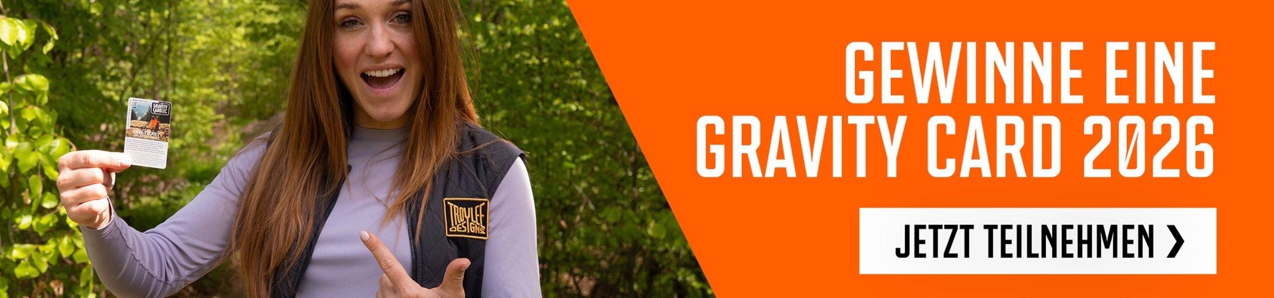 Person hält eine Gravity Card 2026 im Wald und zeigt auf das Ticket für Bikepark- und Trail-Zugang, Gewinnspielmotiv im Outdoor-Setting.