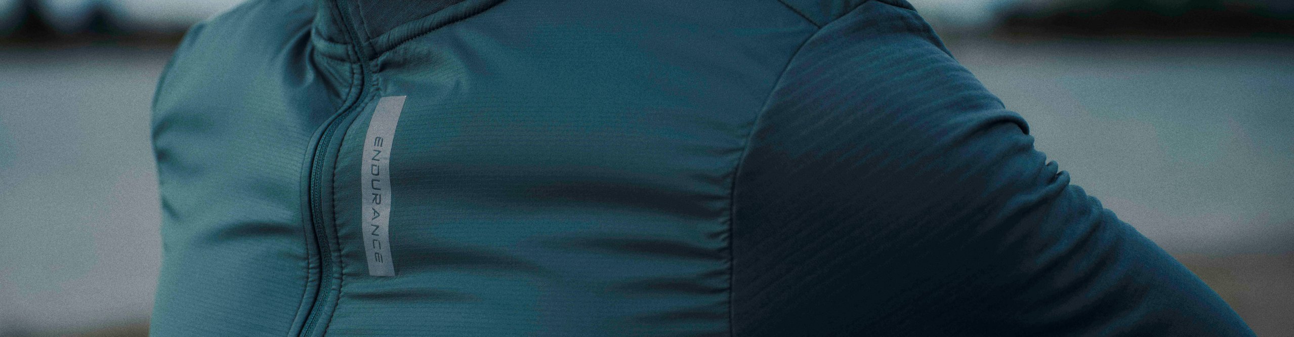Nahaufnahme eines Mannes in einem blaugrünen Endurance Fahrradtrikot mit langen Ärmeln und Stehkragen.