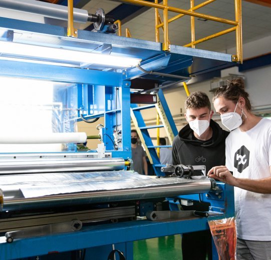 Chris und Ludwig sehen sich die fertigen Carbonmatten, die aus einer Maschine ausgegeben werden, an. 