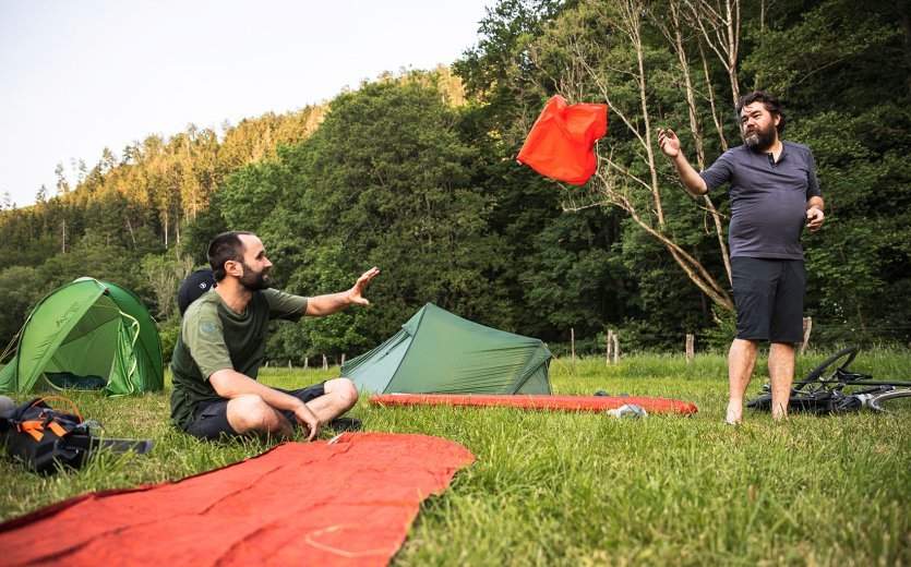 Christian from bc throws a pump bag to his colleague. There are two camping mats, one of which is already filled with air.