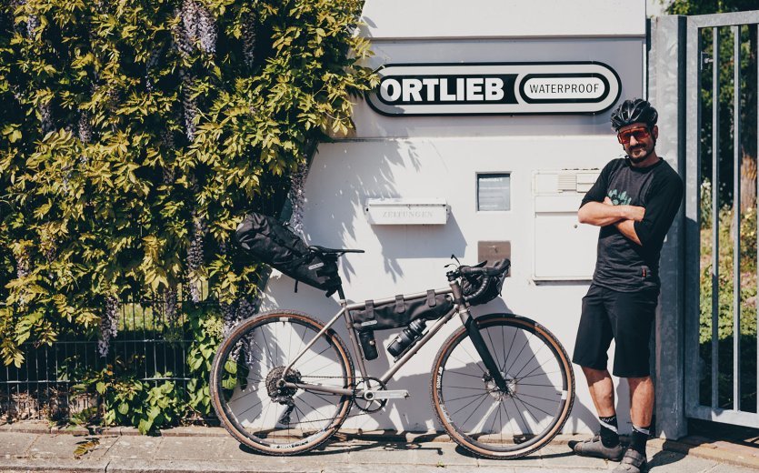 Andi steht samt Gravelbike an der Pforte von ORTLIEB.