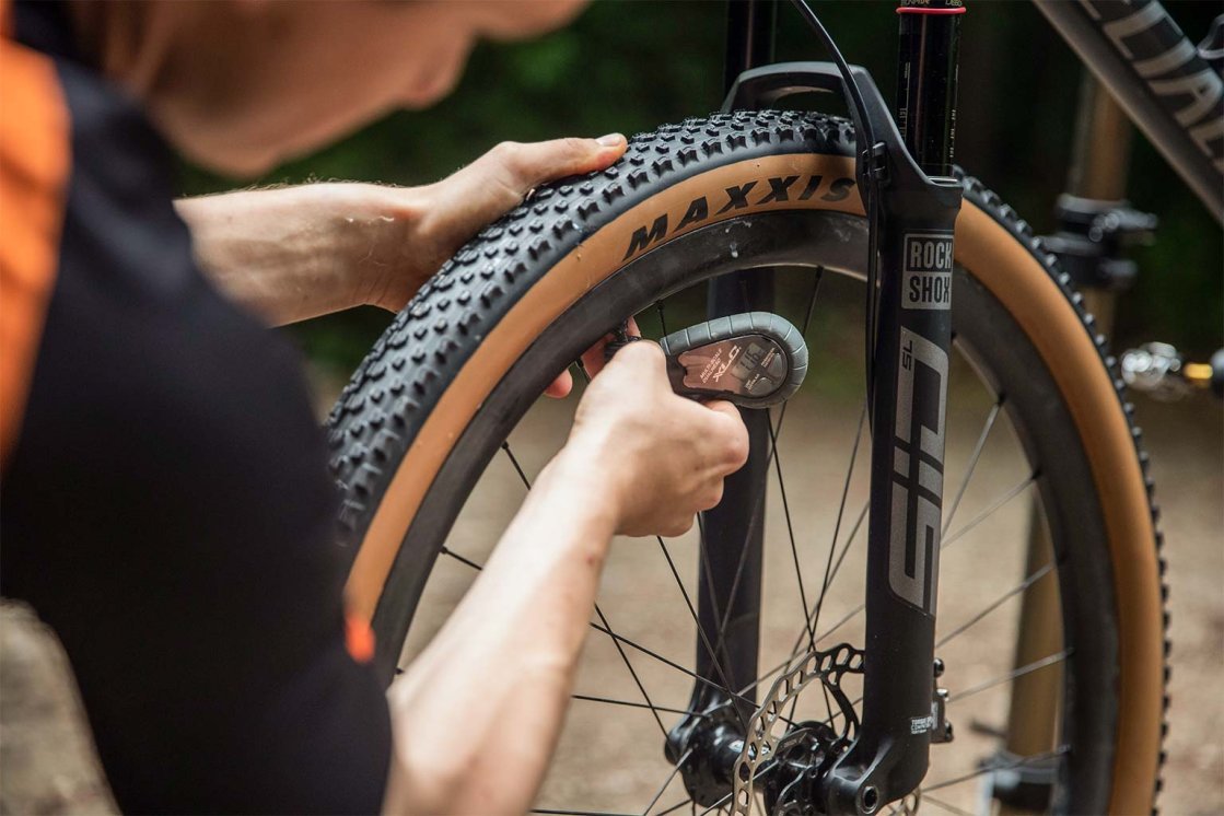 Ciclista de montaña comprobando la presión del neumático en la rueda delantera con un medidor digital.