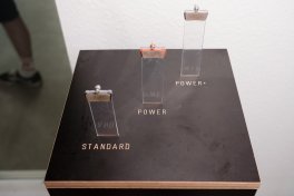 Three transparent tubes containing brake pads are placed on a black surface labeled with "POWER" and "STANDARD."