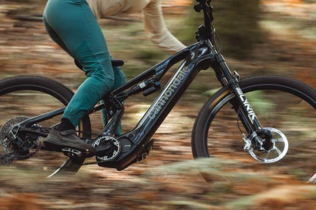 A woman on an E-MTB speeds through the forest. Close-up side view of the bike, rider partially cut off