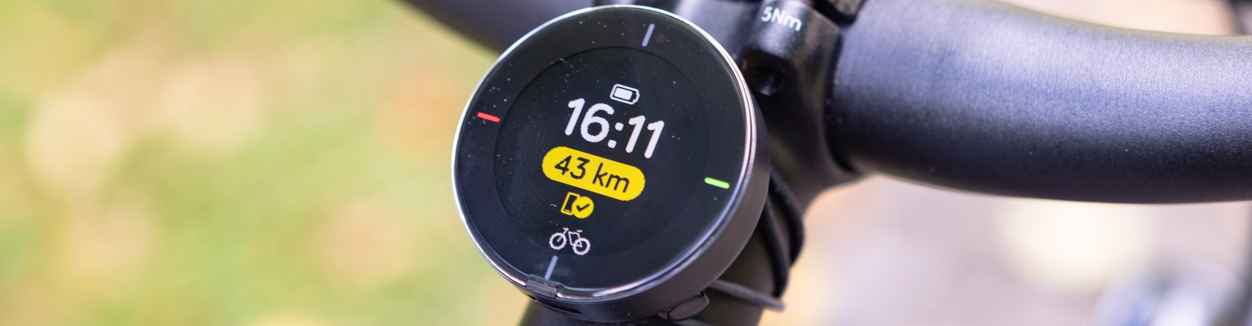 Nahaufnahme des runden Beeline-Fahrradcomputers am Lenker, der Uhrzeit, Akkustand und verbleibende Strecke anzeigt – intuitives Navigationsgerät für moderne Bike-Touren.