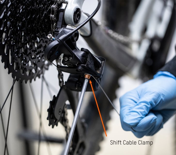 While the bc mechanic tightens the clamp bolt with a hex key, he pulls the shift cable with his other hand.