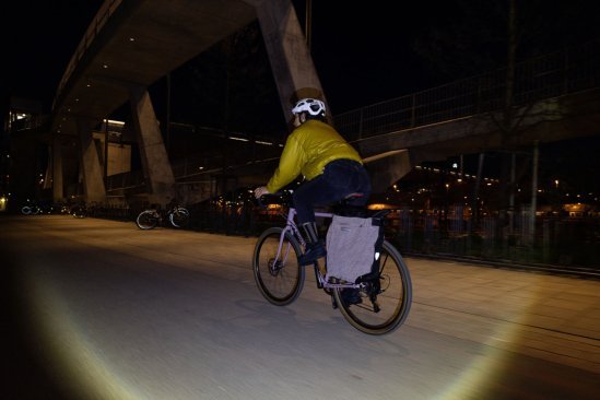 Eine Frau auf einem Rennrad bei Nacht. Der weiße Helm und die retroreflektierende Radtasche sind gut erkennbar.