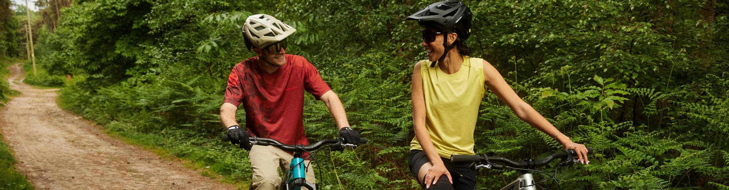 Two mountain bikers wearing Endura apparel and helmets riding relaxed on a forest trail while talking during their ride on mountain bikes.