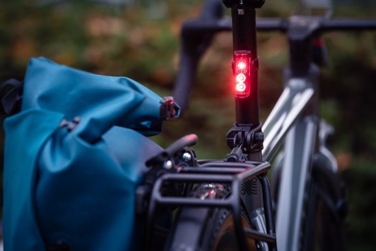 Eine Sigma Rückleuchte mit eingeschaltetem Bremslicht an der Sattelstütze eines dunklen Fahrrads