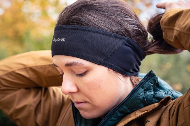 A young woman in a sand-coloured rain jacket pulls her ponytail through a black headband.