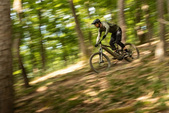 Berno heizt mit dem Turbo Levo 4 E-MTB durch den Wald. Die Umgebung ist durch die Mitzieheraufnahme unscharf, nur Bike und Rider sind scharf und erkennbar.