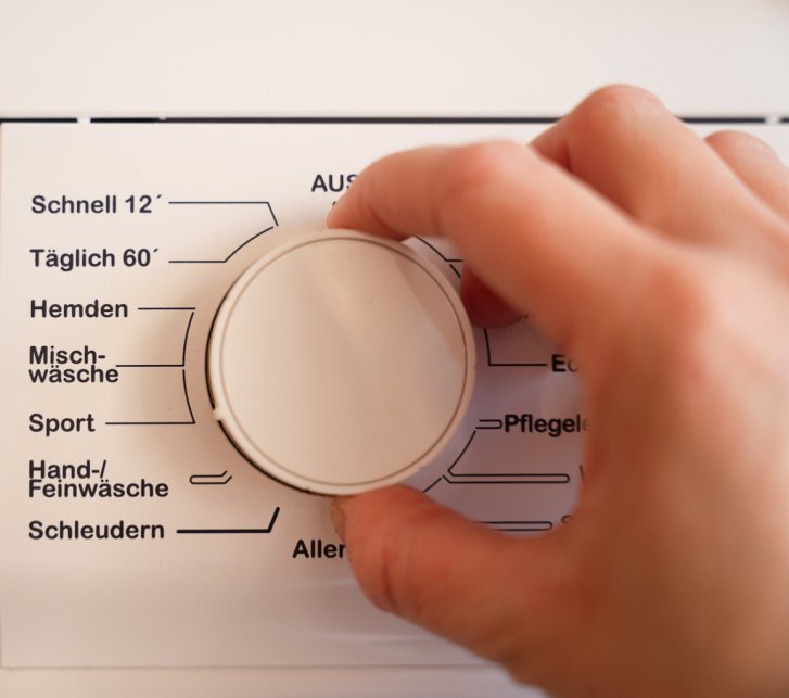 Das Programmwahlrad einer Waschmaschine. Eine Hand stellt das Sportprogramm ein.