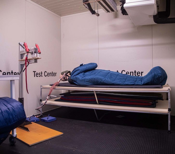 A standard mannequin lies in a VAUDE sleeping bag in a controlled climate chamber at the VAUDE Test Centre. The heat loss of the doll is being measured.