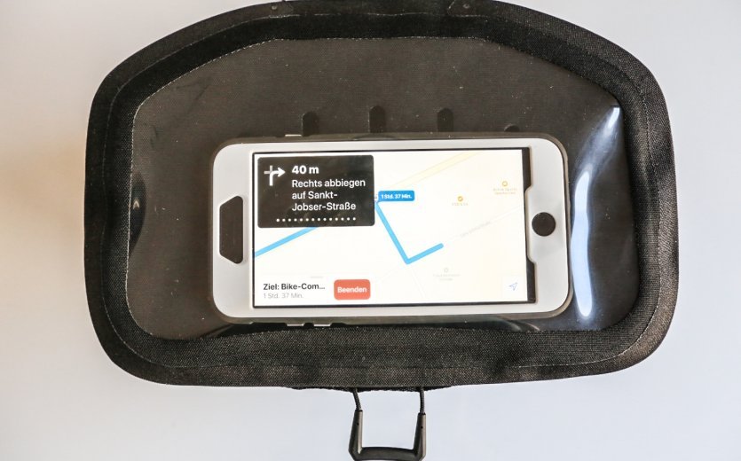 A black bicycle bag with a transparent compartment holding a smartphone displaying a navigation app. 