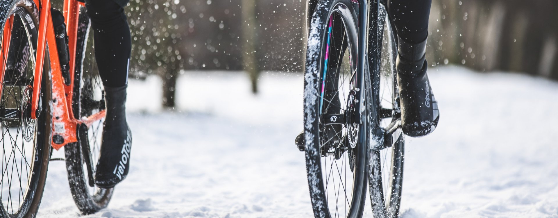 Dos pares de pies pedalean sobre bicicletas gravel hacia la cámara en un paisaje nevado.