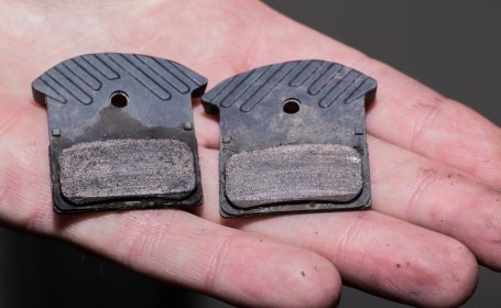 Gros plan d’une main tenant deux plaquettes de frein à disque de vélo fortement usées.