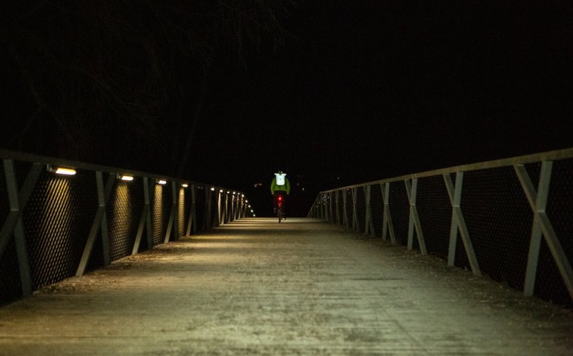 Radfahrer bei Nacht auf Brücke, gute Sichtbarkeit dank Lichtreflexion.