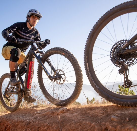 Zwei Mountainbiker, einer davon auf einem Liteville 301 E-Bike, fahren bei sonnigem Wetter in der Nähe der Küste über einen Trail.