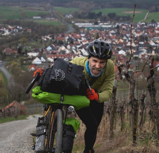 Ein Teilnehmer schiebt mit schmerzverzerrtem Gesicht sein Bike den Weinberg hoch. Man sieht im Hintergrund, wie unfassbar steil die Passage ist. 