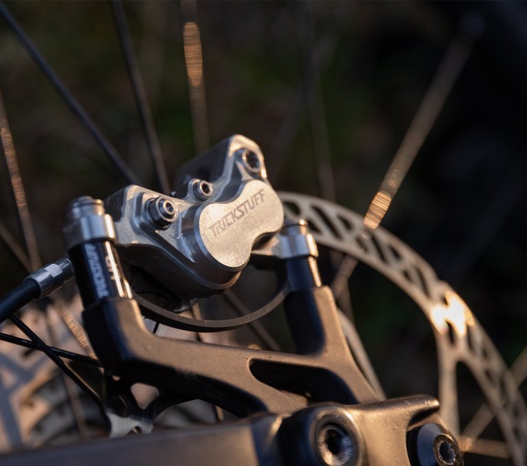 Close-up of a Trickstuff bike component on a mountain bike wheel with a brake disc, illuminated by warm light.