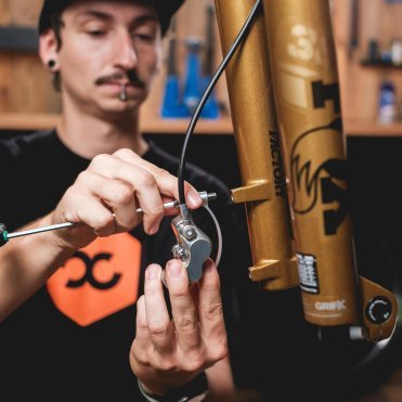 Mecánico instalando una pinza de freno de disco en una MTB con horquilla FOX Factory dorada (Kashima), primer plano en el taller.