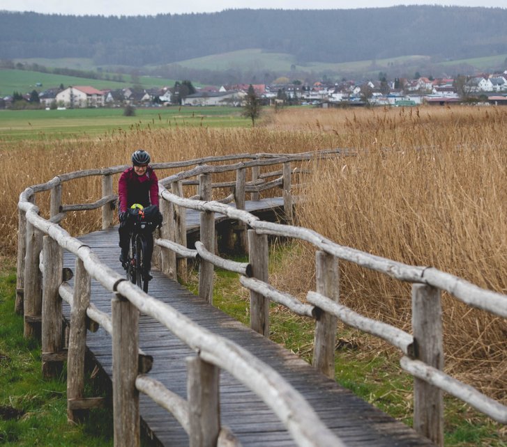 Linda fährt über einen Steg, der durch eine Moorlandschaft führt. 