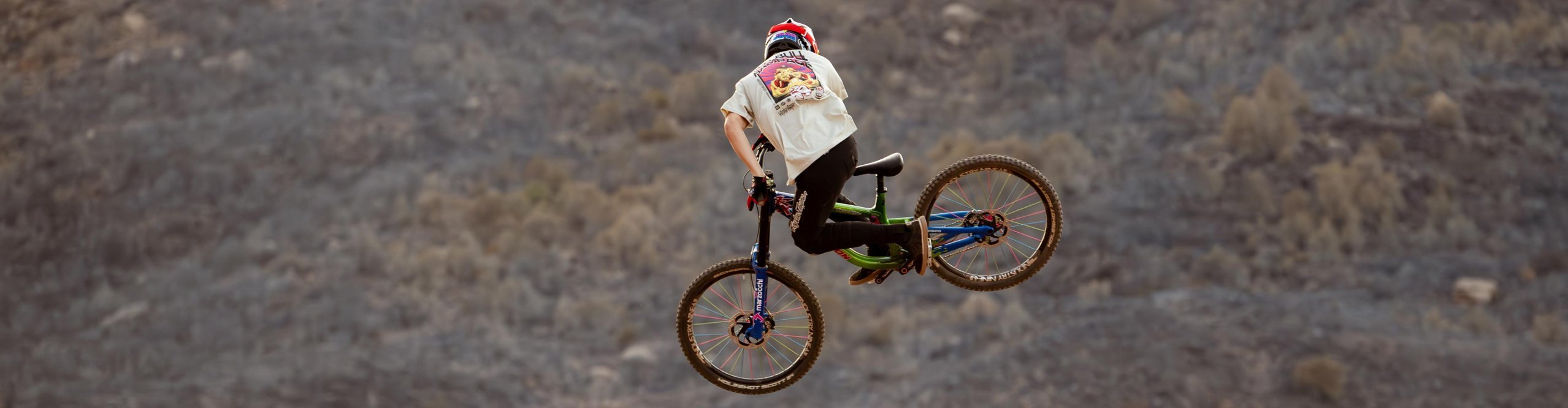 Troy Lee Designs mountain biker performing a freestyle jump on a freeride MTB in a rocky desert landscape