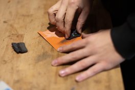A hand roughens a brake pad with sandpaper on a workbench.