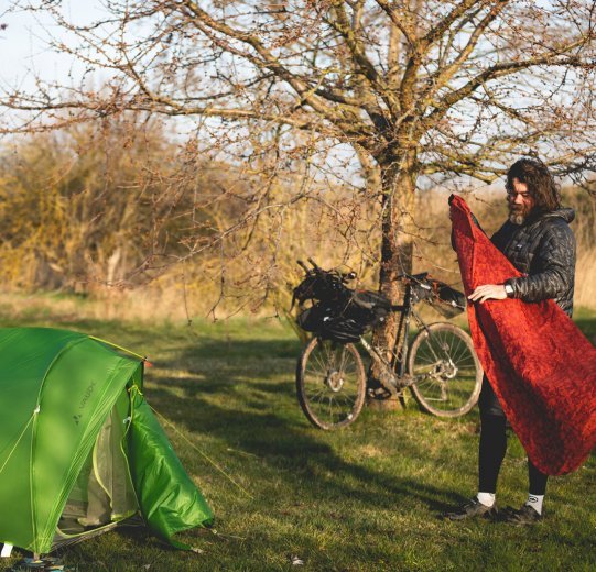 Christian, du service clientèle de bc, replie son matelas de camping. Au premier plan se trouve sa tente, à l'arrière-plan son vélo.