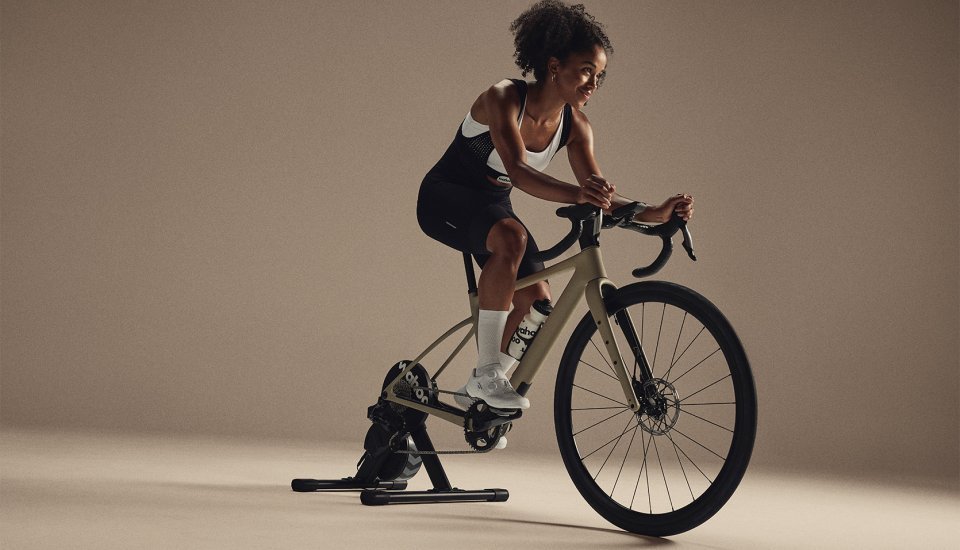 Sportliche Frau trainiert auf einem Rennrad, das auf dem Wahoo KICKR Core V2 Rollentrainer montiert ist, in einem minimalistischen Indoor-Setup.