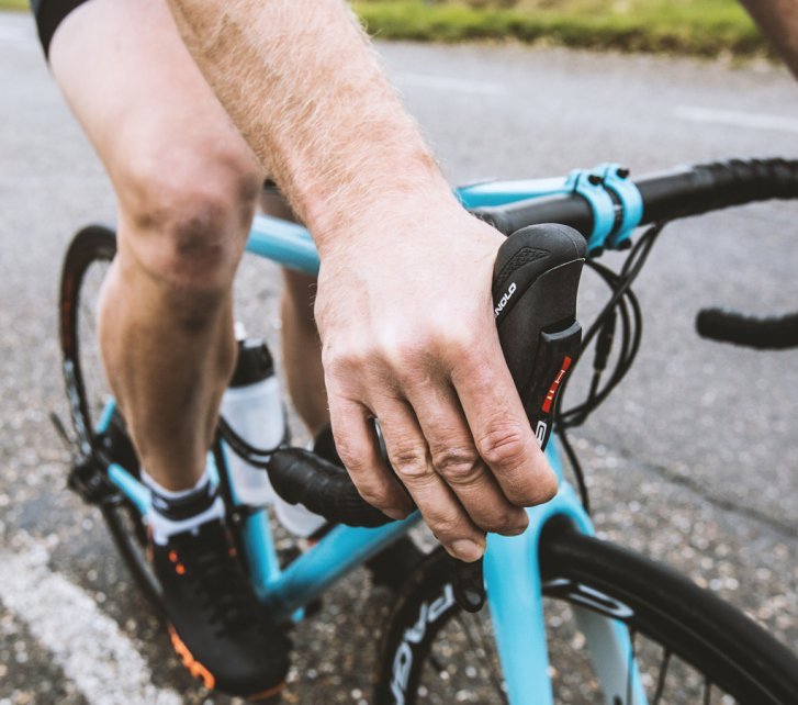 Un ciclista de ruta va con las manos posicionadas en las manetas de frenos mientras frena. 