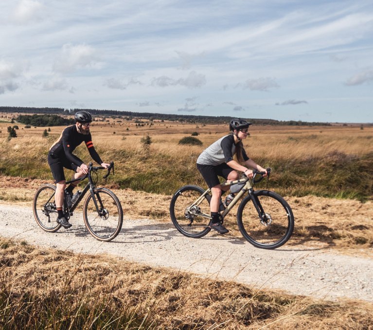 Ein Mann und eine Frau fahren mit ihren Gravelbikes durch eine Feldlandschaft.