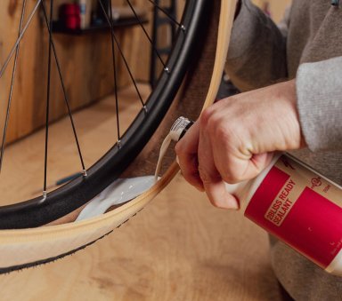 Main versant du liquide préventif dans le flanc ouvert d’un pneu déjà monté sur la jante.