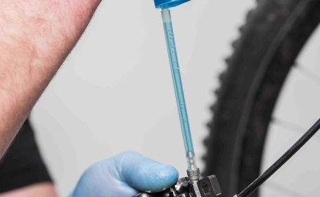 Luftblasen steigen aus einer Bremszange durch einen Plastikschlauch in eine Einwegspritze mit klar-blauer Bremsflüssigkeit